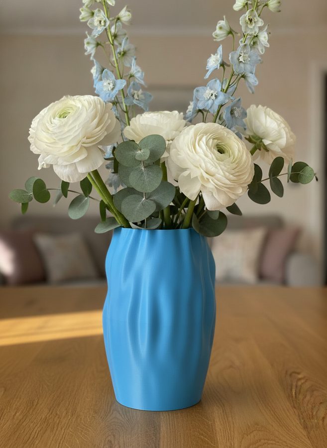 The same vase on a table holding white ranunculus, eucalyptus and pale blue delphinium in a softly blurred living room
